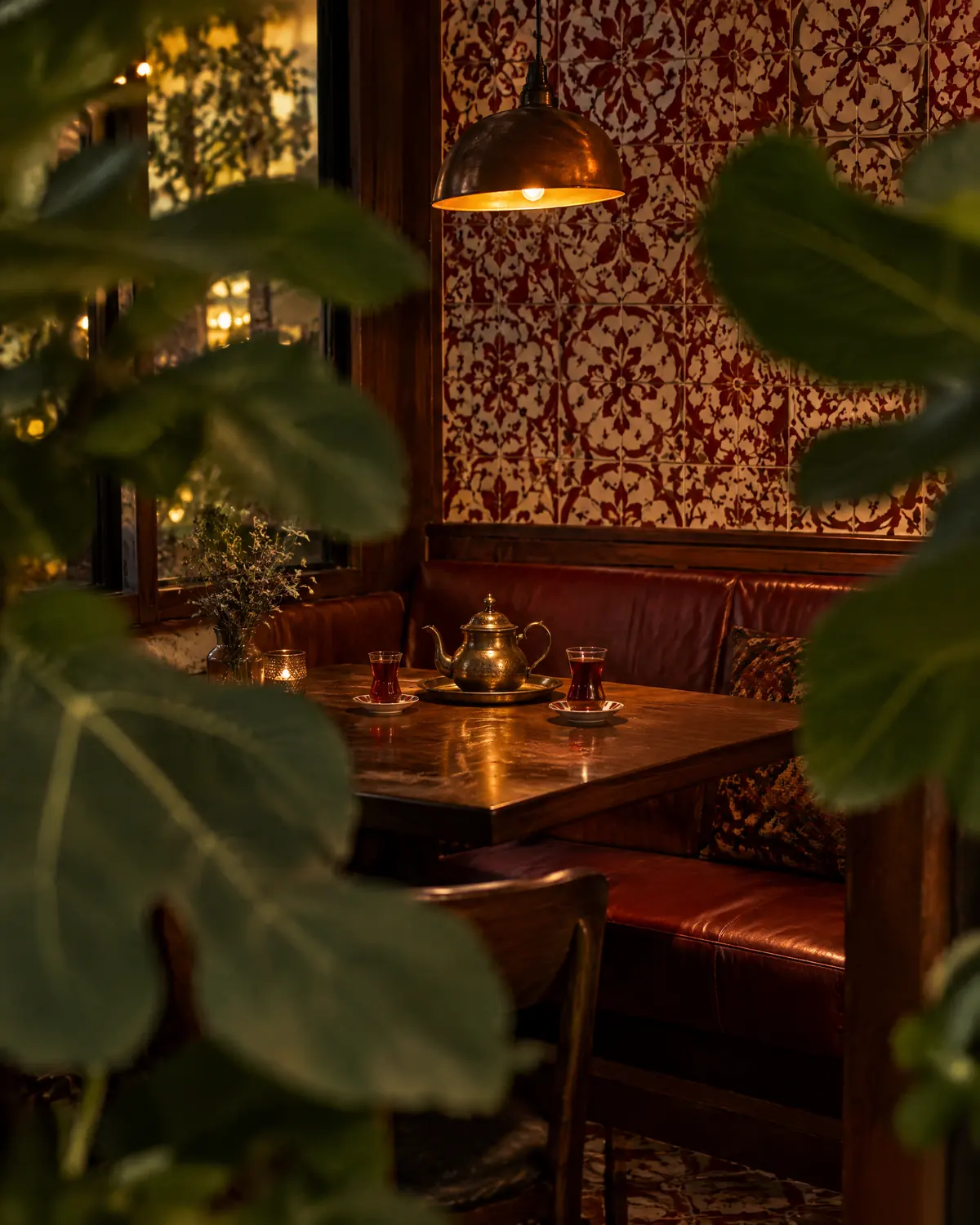 A booth with a teapot and tea glasses seen past large fig leaves